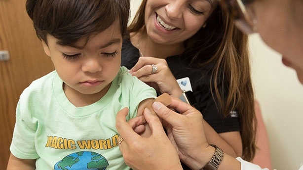 A close-up image of a doctor applying a band-aid on a boy's arm after giving him a shot administered by his mother.
